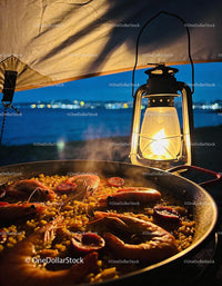 Seafood paella simmering by lantern light at dusk