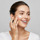 Young Woman Applying Skincare Cream with Bright Smile in Studio