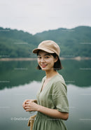 Young Woman in Green Dress Wearing Beige Cap Near Lake Landscape