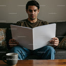 Young man reading large book while sitting on sofa