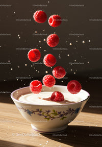 Fresh raspberries falling into creamy yogurt bowl