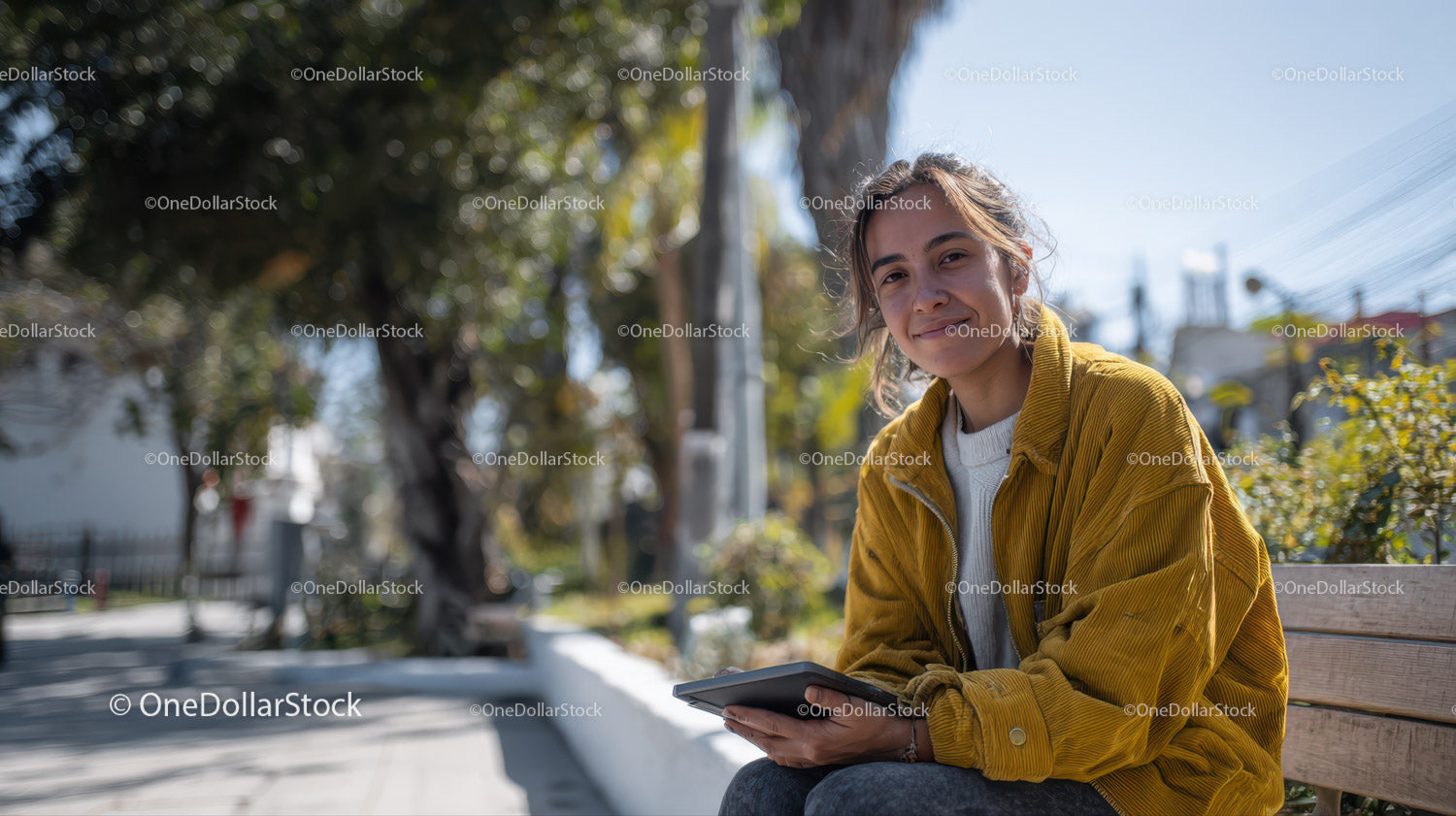 Young Woman in Yellow Jacket Sitting on Bench Using Digital Tablet