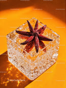 Star anise embedded in clear ice cube on orange surface