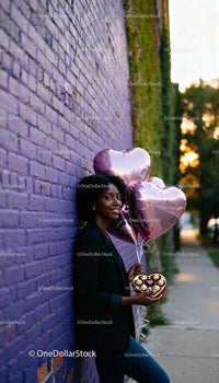 Smiling woman holding heart balloons and chocolates outdoors