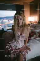 Stylish Young Woman in Pink Satin Dress Sitting on Bed in Bedroom
