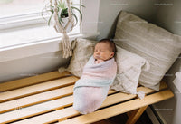 Peaceful newborn wrapped in pastel blanket by window
