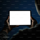 Person holding illuminated digital tablet in dark room