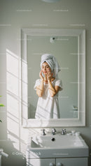 Woman in Bathroom with Towel Touching Face Looking in Mirror
