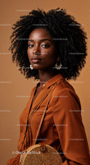 Elegant Woman with Curly Hair in Brown Outfit Standing Against Warm Background