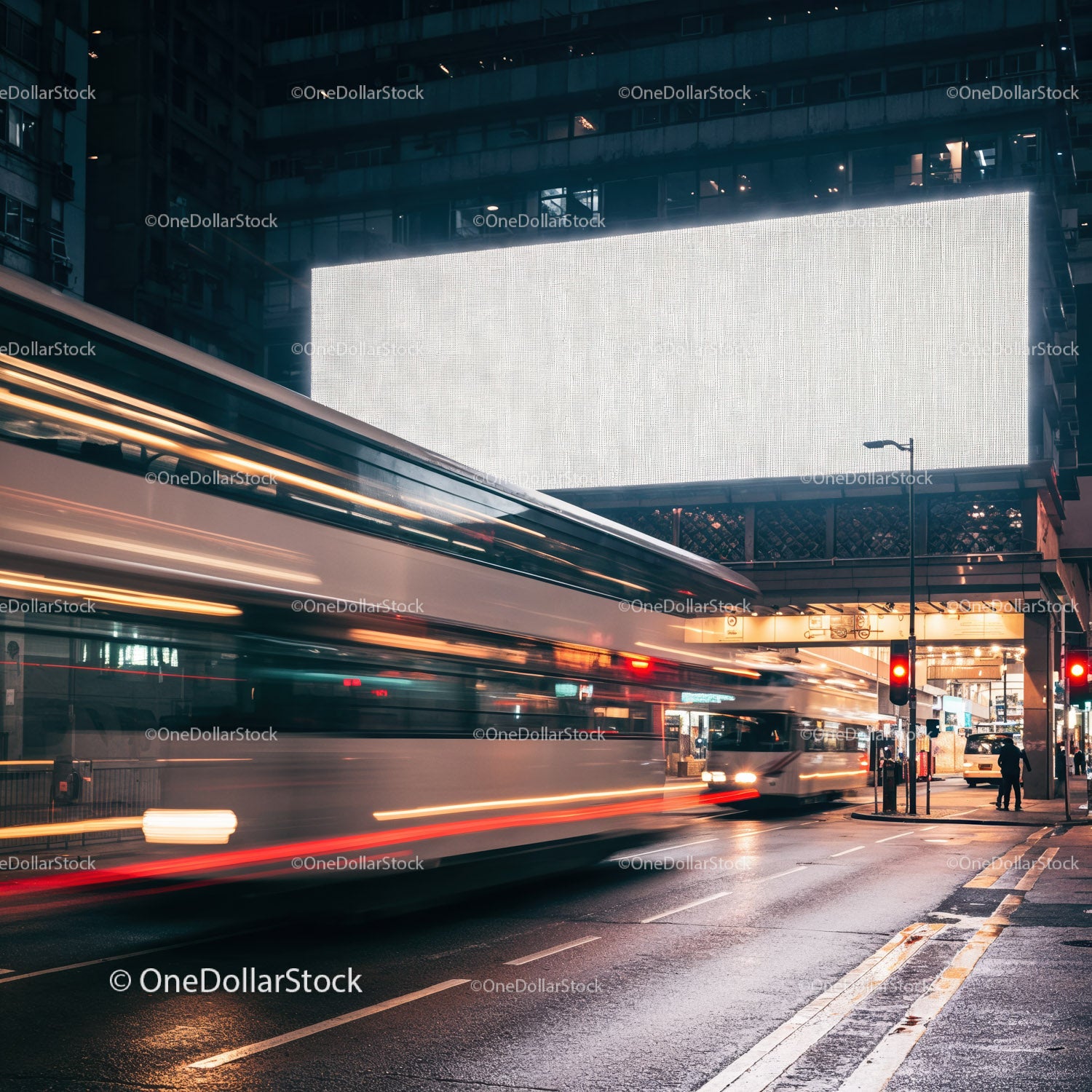 Autobusy miejskie przejeżdżające nocą pod dużym, oświetlonym billboardem