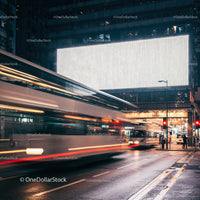 City buses passing under large illuminated billboard at night