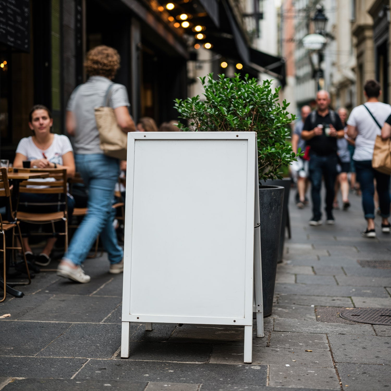 Blank sidewalk sign in bustling city street cafe scene
