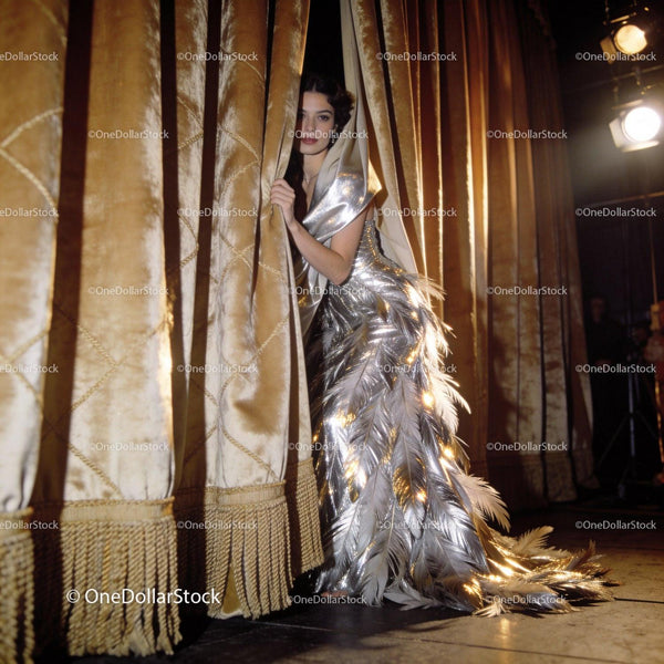 Elegant woman in shimmering feathered gown behind curtain