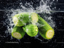 Fresh Green Zucchini Splashed with Water Against Black Background