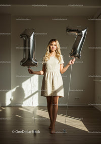 Young woman holding silver 17 balloons indoors