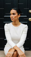 Elegant woman in white dress sitting by black door
