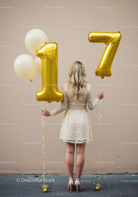 Woman celebrating seventeenth birthday with gold balloons
