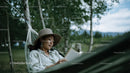 Woman Relaxing in Hammock Reading Book Under Green Trees