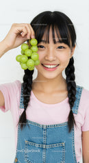 Smiling Girl with Pigtails and Green Grapes on Bright Background