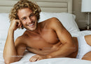 Smiling young man relaxing on bed in white underwear