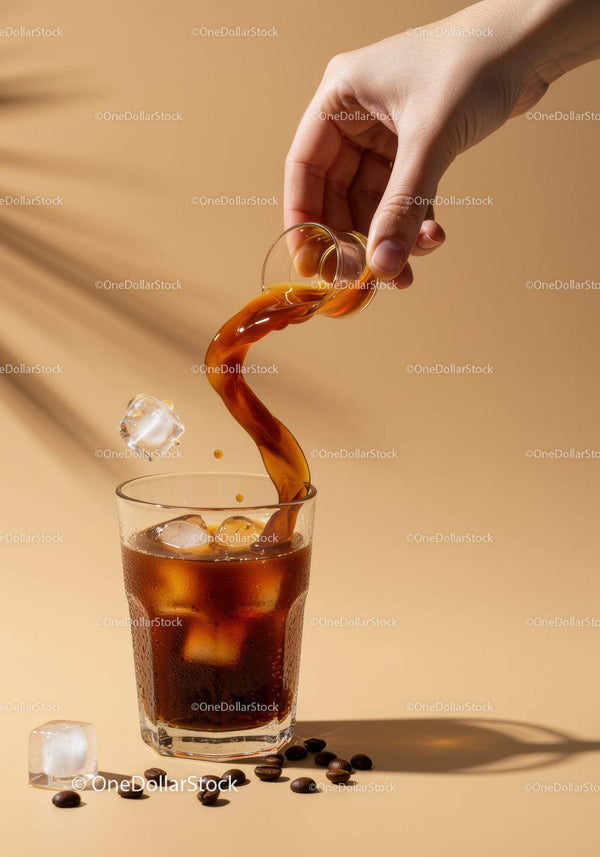 Hand pouring cold brew coffee over ice in glass