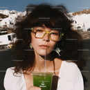 Stylish Woman with Curly Hair and Yellow Sunglasses Drinking Green Beverage