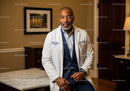 Professional Senior Male Doctor in White Coat Sitting in Modern Clinic