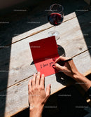 Man writing love message in red card by wine glass
