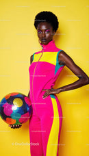 Stylish Woman in Bright Sporty Outfit Holding Colorful Ball Against Yellow Background