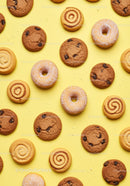 Assorted cookies and powdered donuts on yellow background