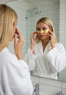 Young Woman Applying Under-Eye Patches in Bathroom Mirror