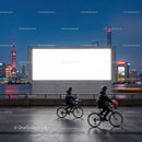 Cyclists Passing Large Blank Billboard at Urban Waterfront Night
