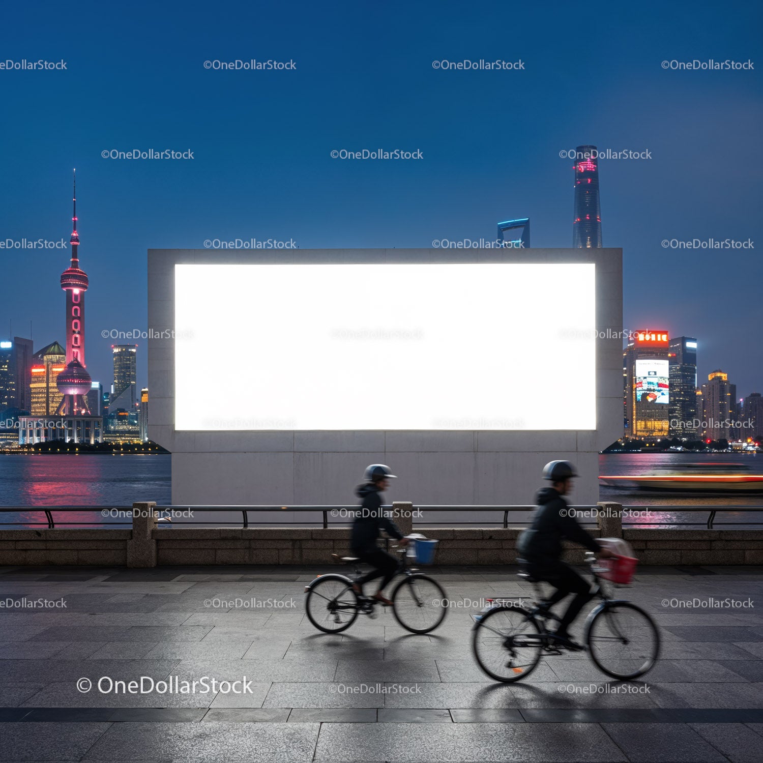 Rowerzyści mijają duży, pusty billboard podczas nocnego nabrzeża miejskiego