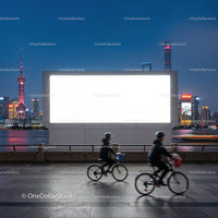 Cyclists Passing Large Blank Billboard at Urban Waterfront Night