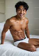 Smiling muscular man sitting on bed in white briefs