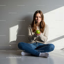 Young woman sitting on floor holding green apple