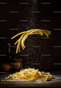 Uncooked pasta with falling flour over dark background