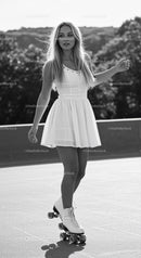 Young woman roller skating outdoors in white dress