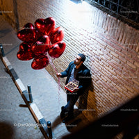 Man standing with heart balloons and chocolates at night