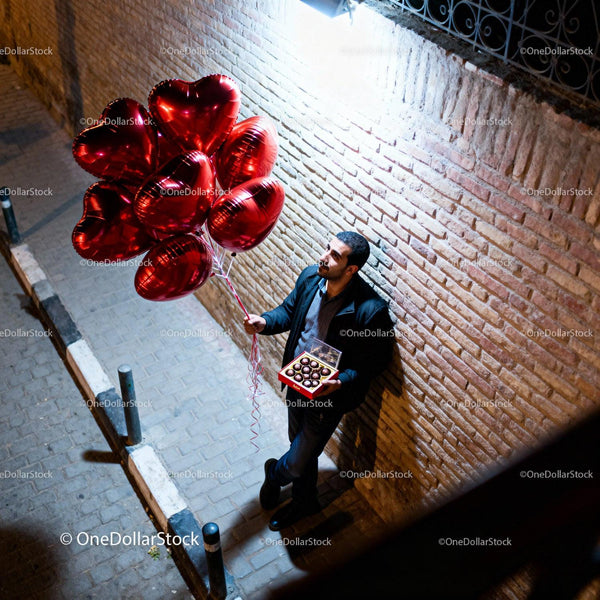 Man standing with heart balloons and chocolates at night