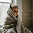 Thoughtful toddler wrapped in cozy blanket by window