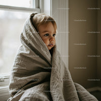 Thoughtful toddler wrapped in cozy blanket by window