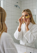 Young Woman Applying Gold Eye Masks in Front of Mirror During Skincare Routine