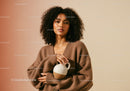 Portrait of a Confident Woman with Curly Hair Holding a Ceramic Vase in Brown Sweater