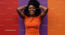 Joyful Black Woman with Curly Hair in Bright Orange Dress Against Colorful Wall