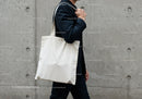 Person carrying blank canvas tote bag walking by concrete wall