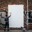 Man painting over graffiti on urban brick wall
