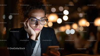 Young woman with glasses using smartphone in cozy cafe at night
