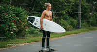 Young man riding skateboard with surfboard in outdoor tropical setting