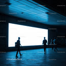 Silhouettes Walking Near Bright Urban Billboard at Night